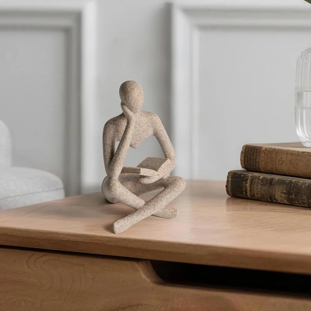 Decorative sculpture of a person in a meditative pose on a wooden surface with books.