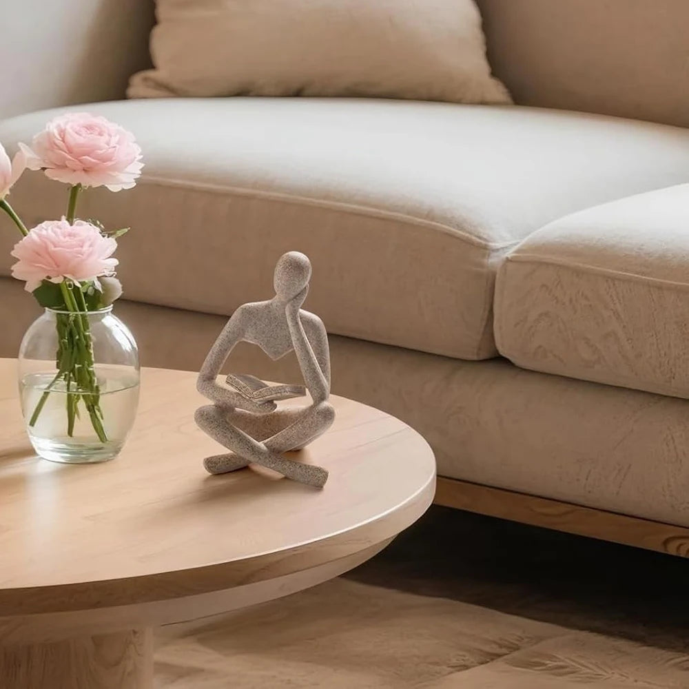 Decorative sculpture of a person sitting on a table with pink flowers in the background