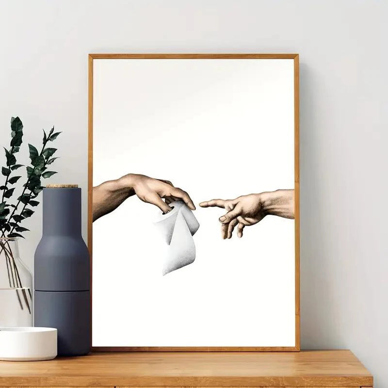 Framed artwork of two hands reaching towards each other on a white wall with decorative items below.
