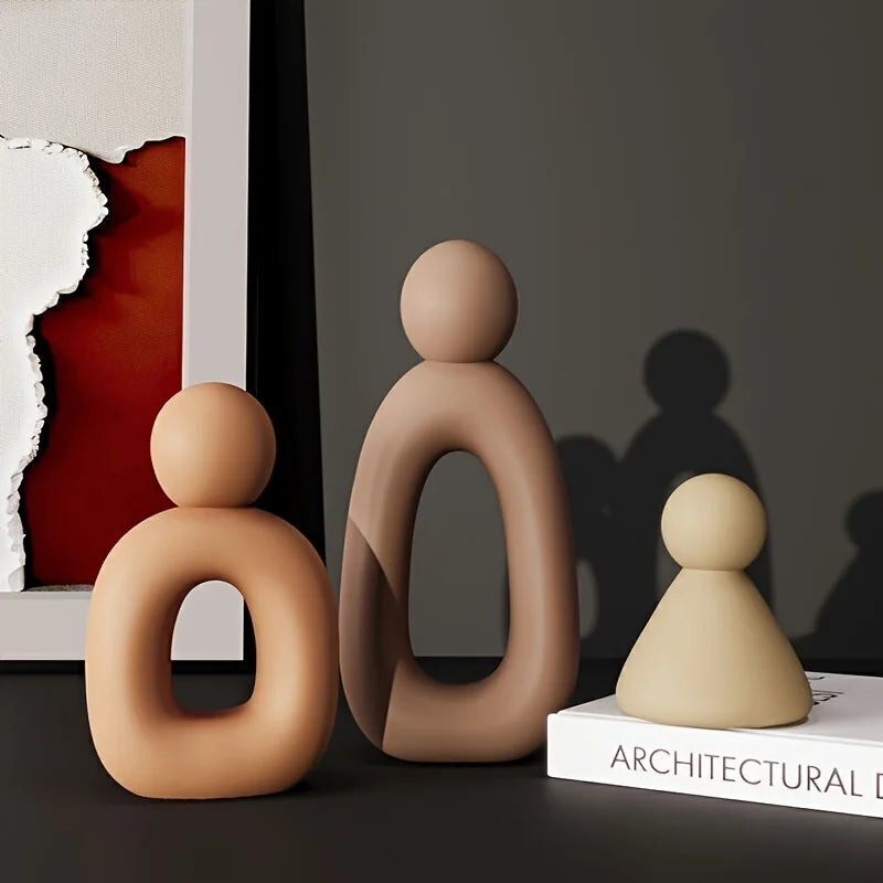 Three brown abstract sculptures on a dark surface with a book titled 'Architectural' in the background.
