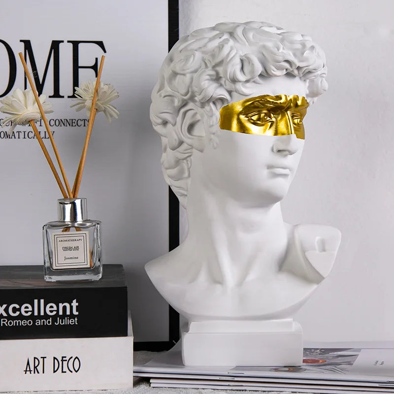 David White marble bust with gold leaf on face next to a decorative bottle and books.